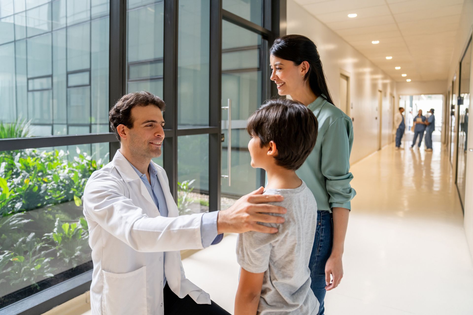 Doctor speaking with a child and parent in a hospital hallway. The doctor has his hand on the child's shoulder.