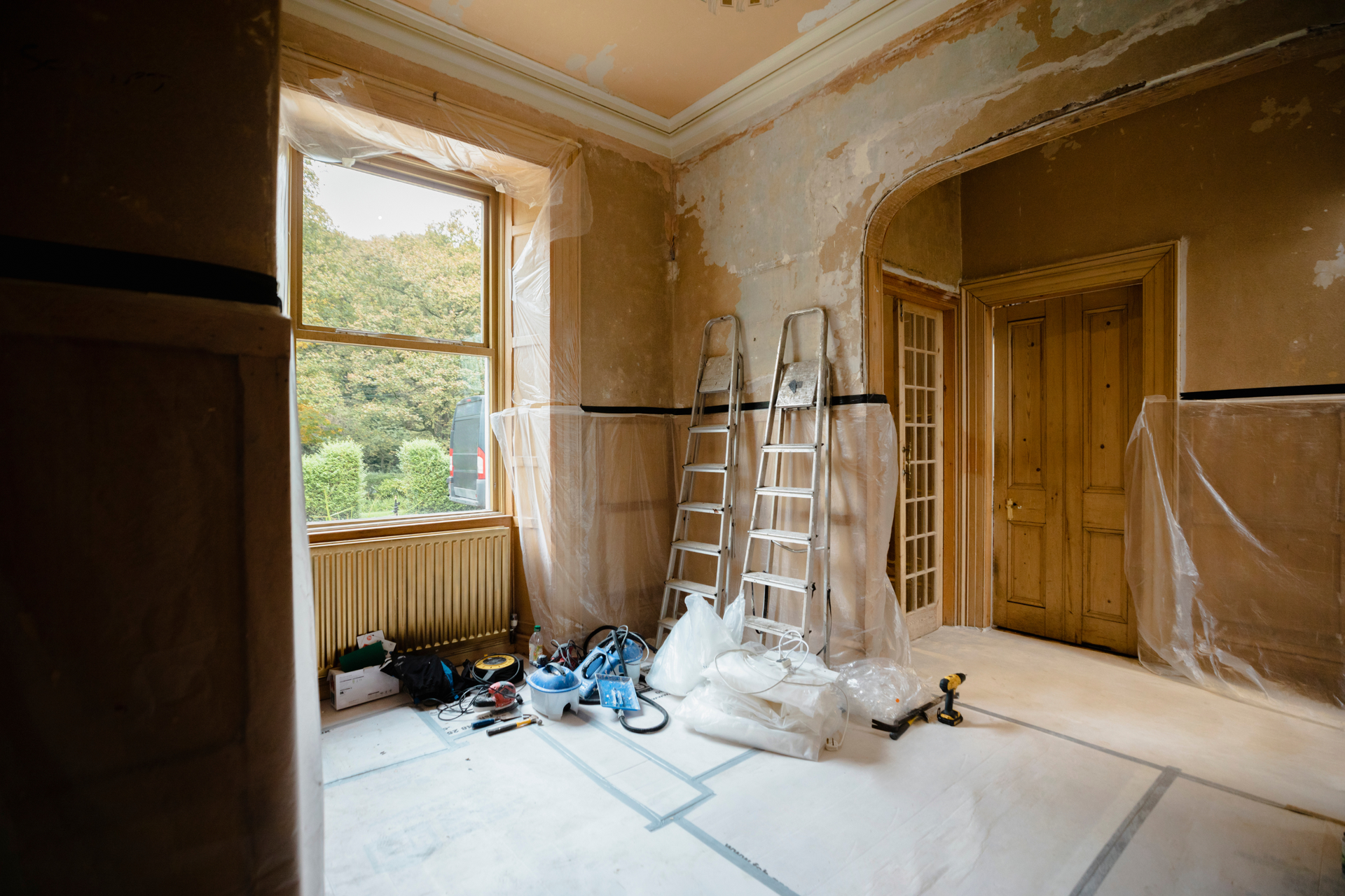 An empty room with a ladder and tools on the floor.