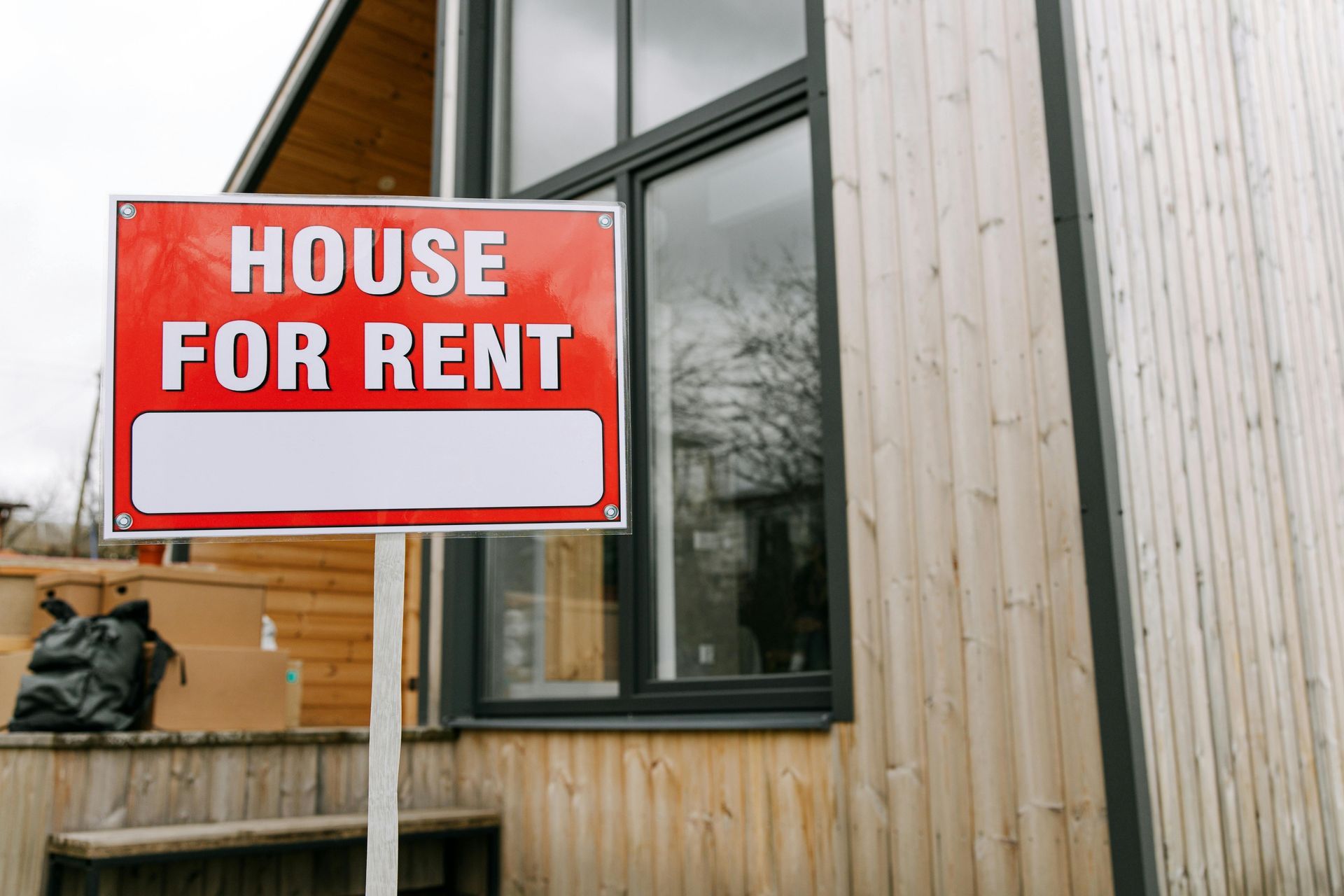 A house for rent sign is in front of a wooden house.