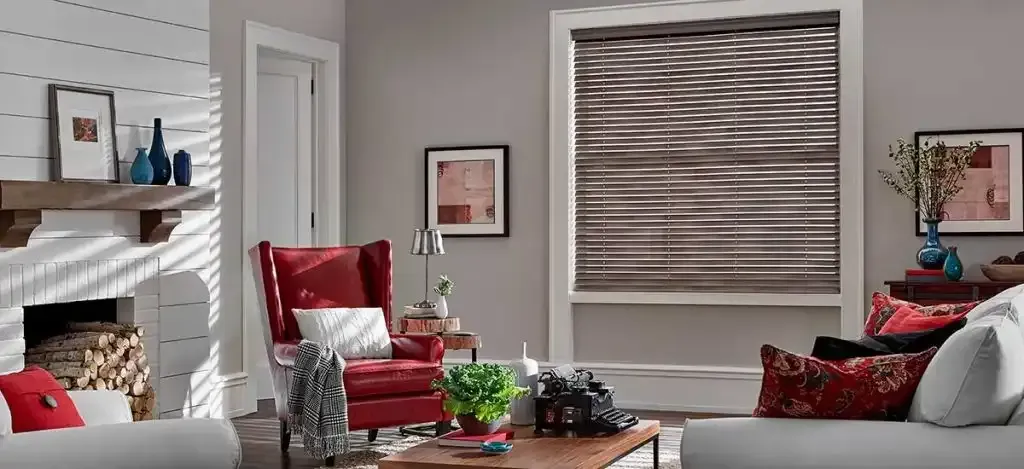 Living room with red armchair, fireplace, window with blinds. Gray walls, brown coffee table, decorative pillows.