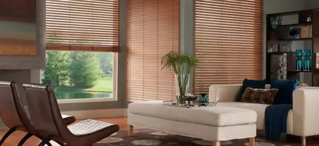 Living room with wood blinds, white couch, and chairs, overlooking a lake.