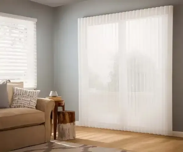 Living room with sheer white curtains on a large window and blinds on a smaller window.