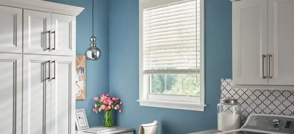 White cabinets in laundry room with blue walls, window, and floral arrangement.