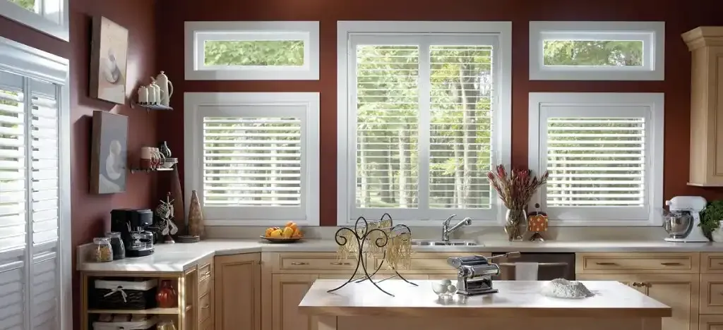Kitchen with red walls, white shutters, and a large window overlooking trees.