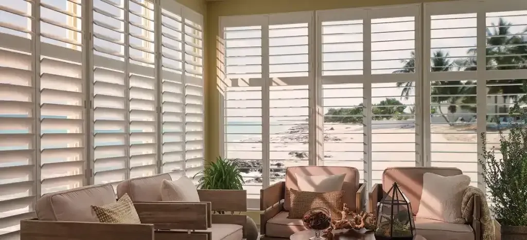Sunroom with white shutters, beach view, and cozy seating.