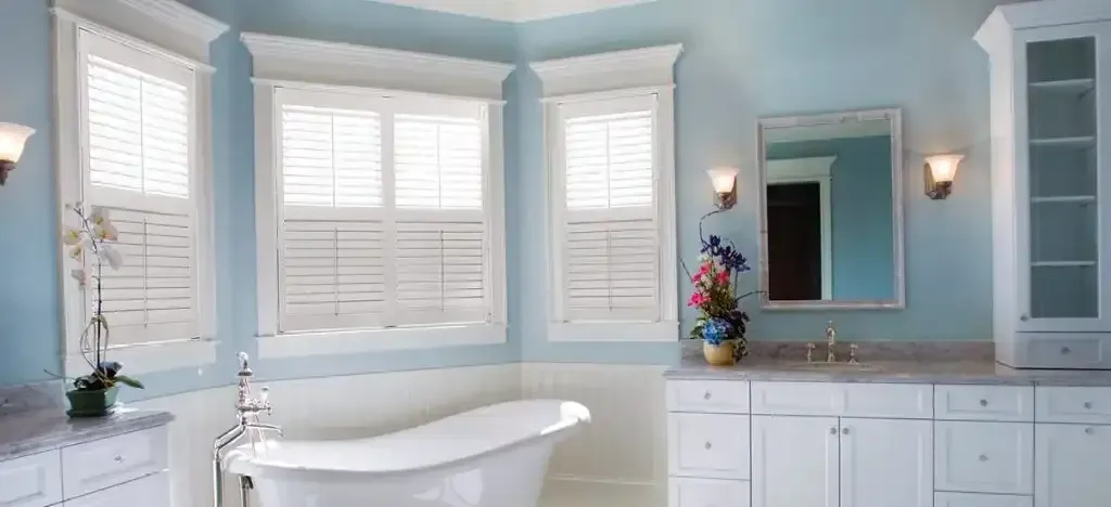 Bathroom with blue walls, white cabinets, a clawfoot tub, and windows with shutters.