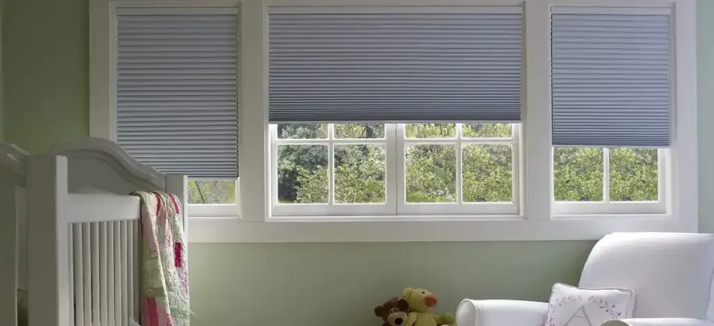 Window blinds in a nursery setting with a crib and a rocking chair.