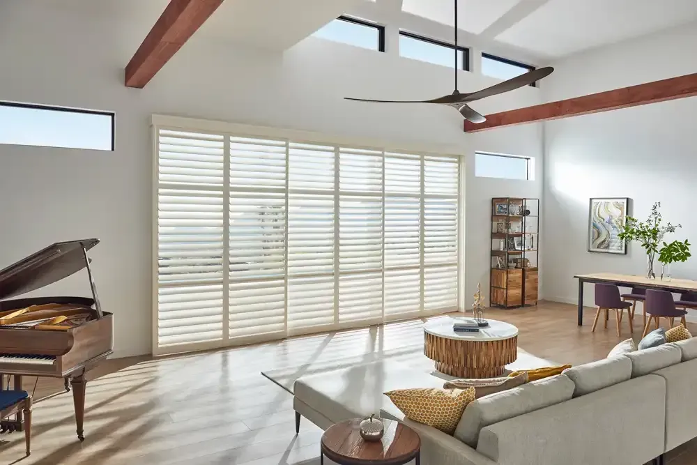 Spacious living room with piano, large windows, and modern furniture. Natural light floods the room.