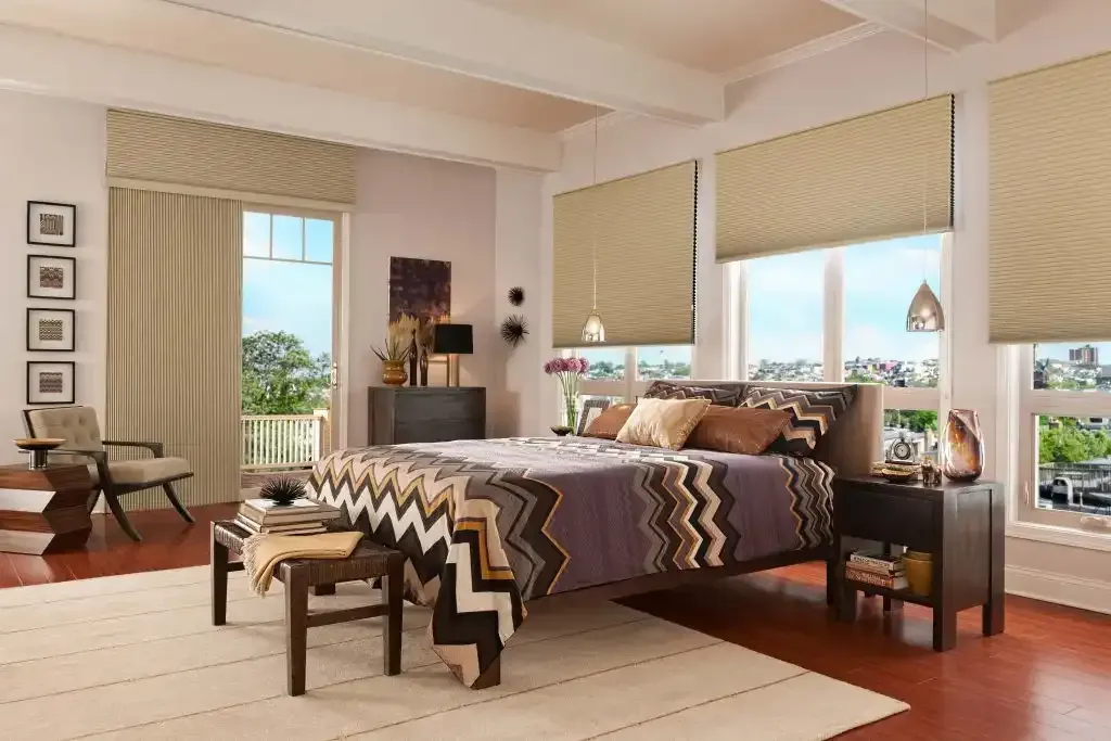 Bedroom with bed, windows, cream blinds, patterned bedding, and wooden furniture.