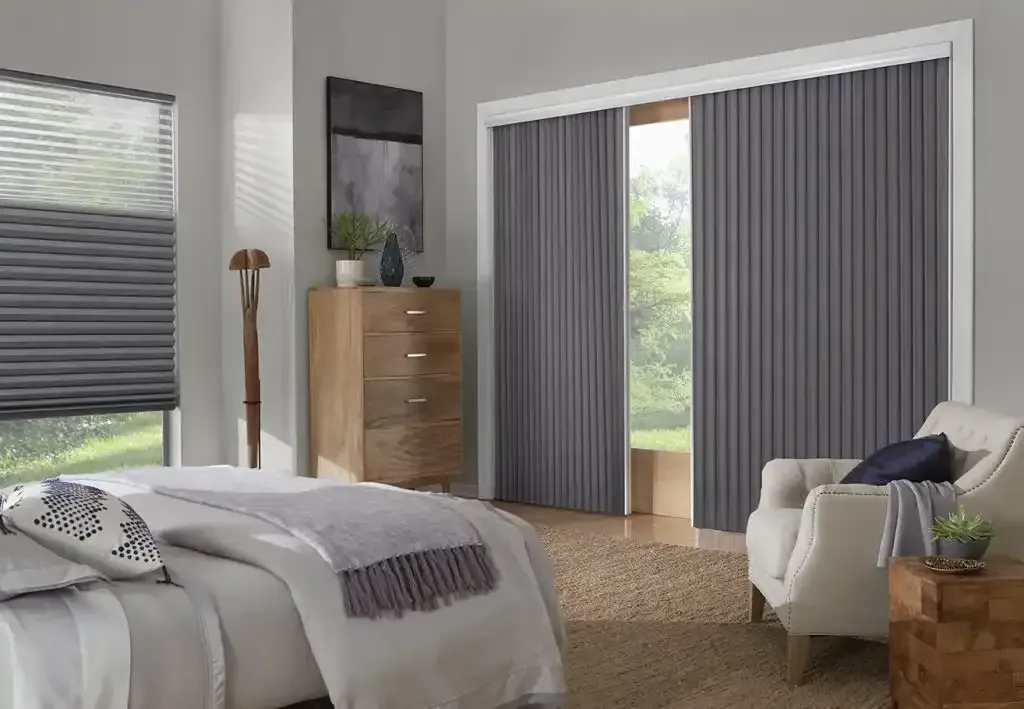 Bedroom with bed, wooden dresser, armchair, and gray window coverings.