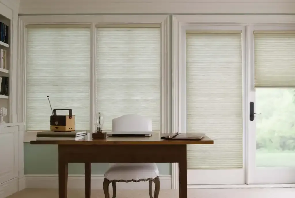Desk in front of three windows with light beige blinds. A radio, lamp, and chair sit on the desk.