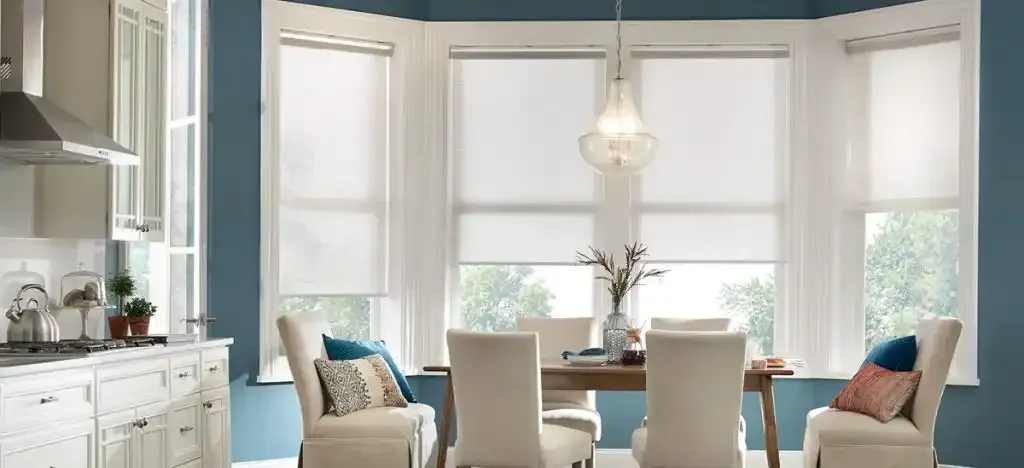 Dining room with white roll-down shades and a chandelier. Blue walls surround a dining table and chairs.