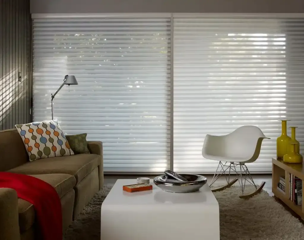 Living room with white sheer blinds, tan sofa, modern chair, and small coffee table.