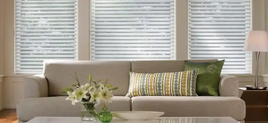 Living room with tan couch, white coffee table, and three windows with white blinds.