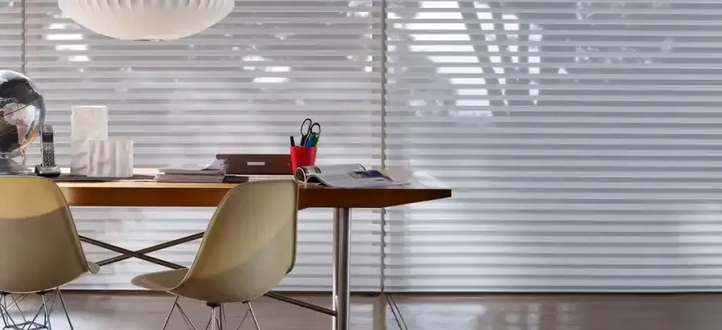 A modern office space with a wooden desk, two yellow chairs, and window blinds casting shadows.