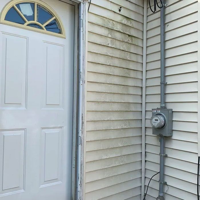White door and siding with green mildew, electric meter, and conduit.