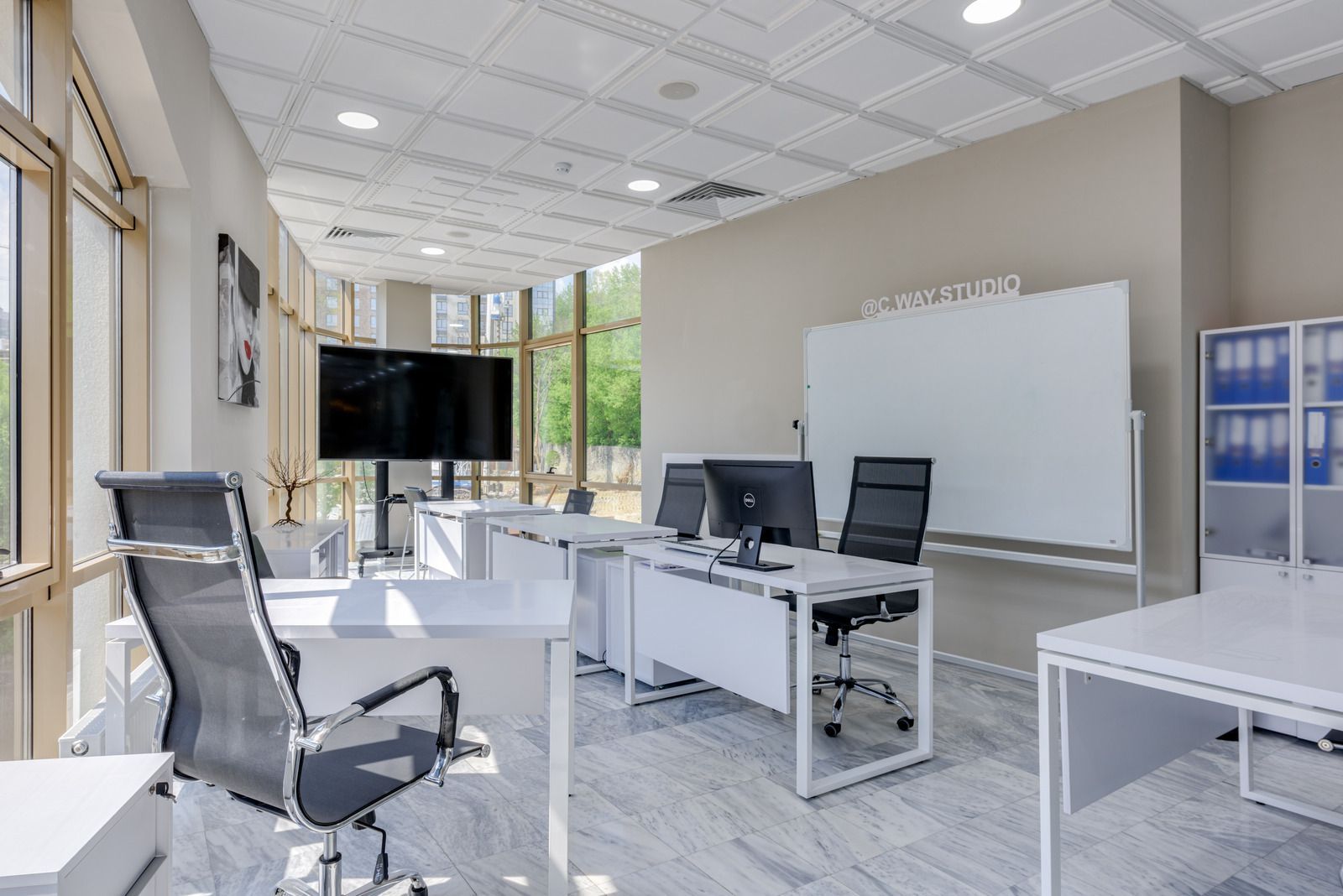 Modern office with white desks, black chairs, large screen, and whiteboard.