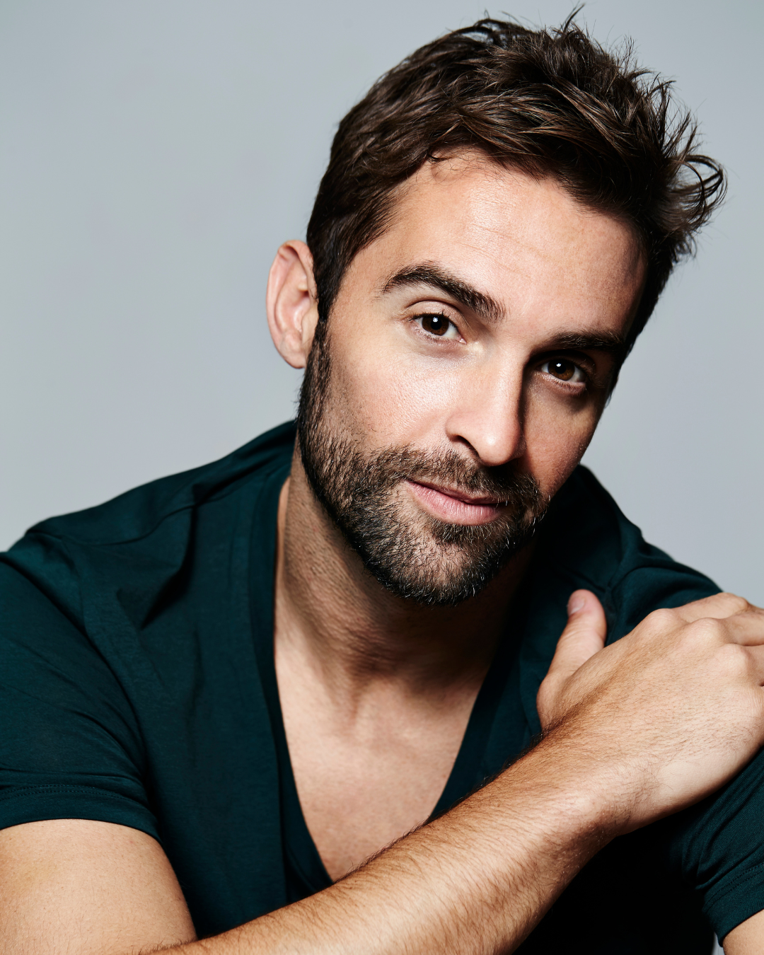 Mann mit dunklen Haaren und Bart in einem dunkelgrünen Hemd, der den Betrachter anschaut.