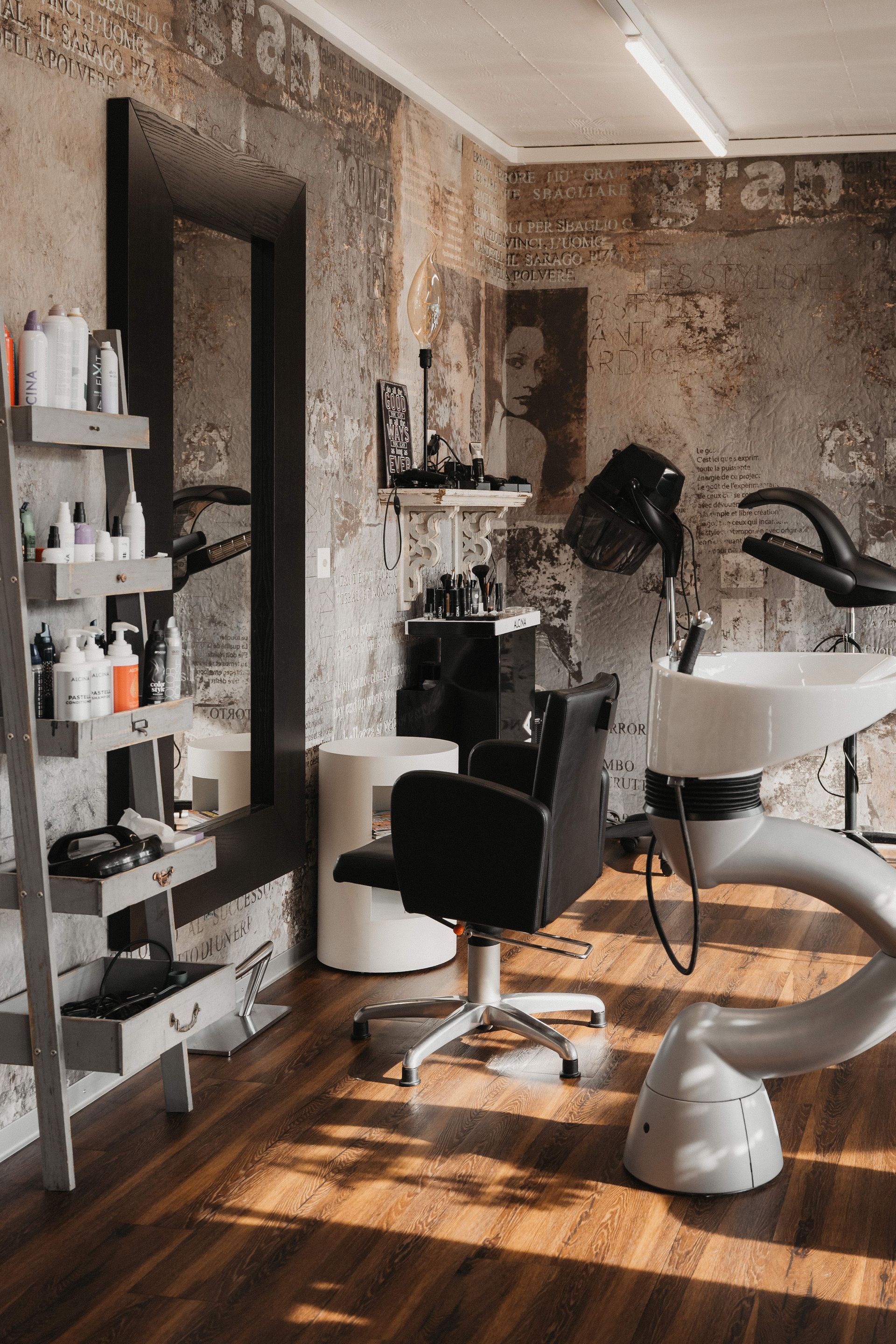 Interieur eines Friseursalons mit Frisierplatz, Stuhl und Produkten in Regalen. Sichtbare Backsteinwand.
