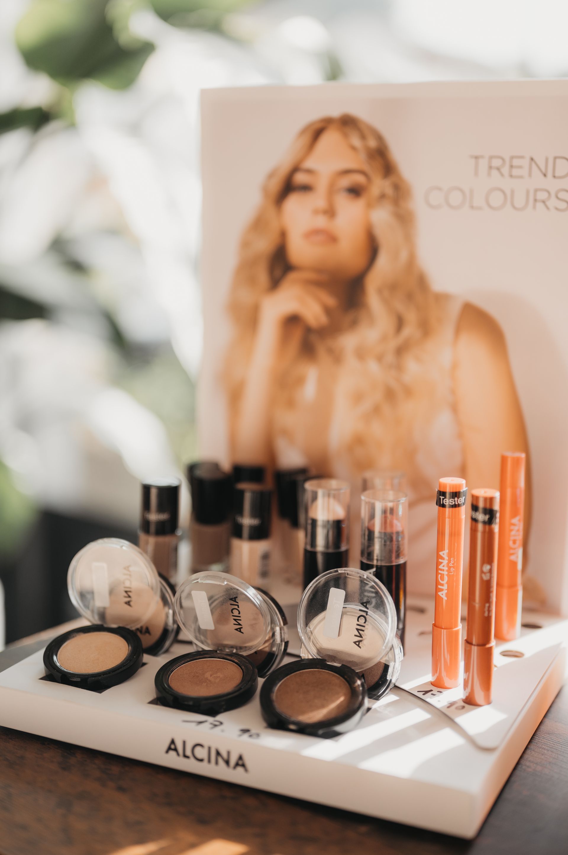 Make-up-Display mit Produkten und einer Frau, das die Marke Alcina präsentiert.
