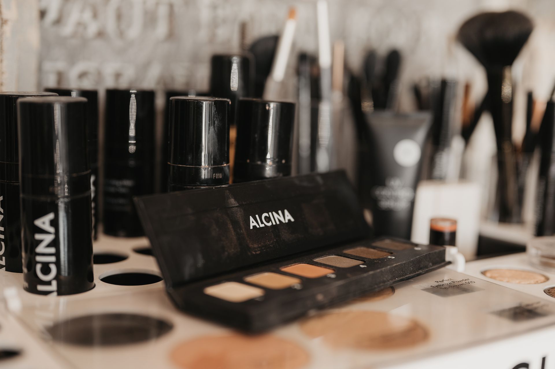 Make-up-Produkte wie Paletten und Pinsel auf einem Regal, neutrale Farbtöne.