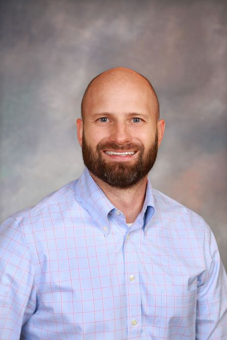 A bald man with a beard is wearing a blue shirt and smiling for the camera.