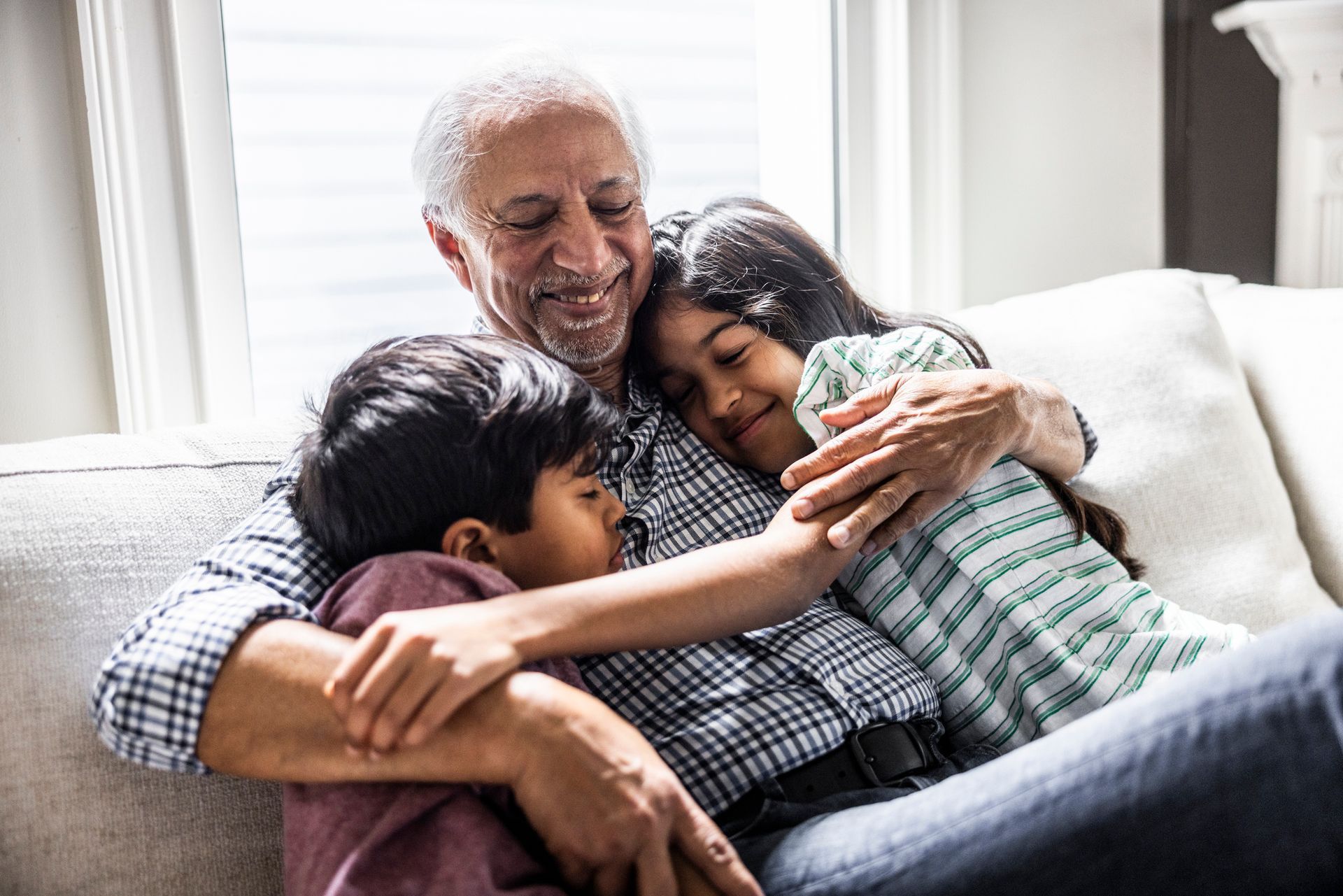 Grandfather cuddling with grandchildren on couch at retirement village.