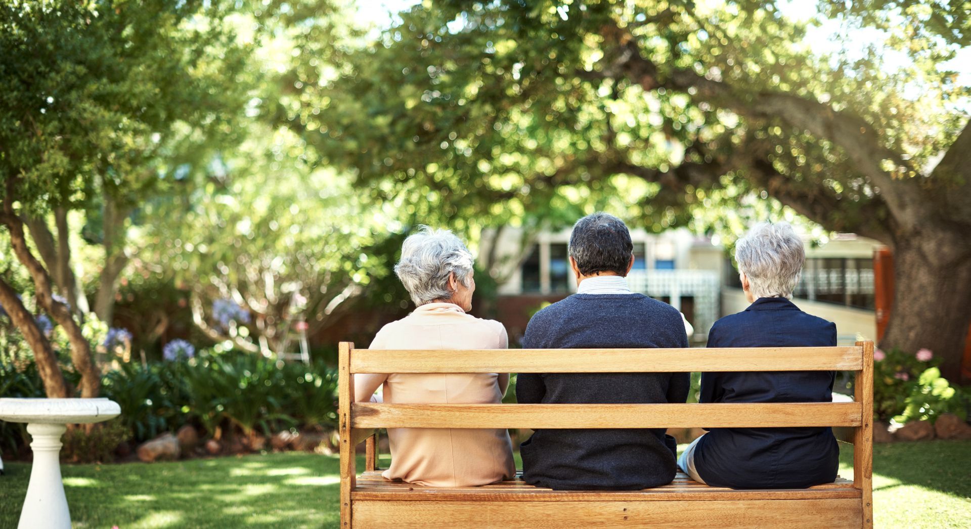 A group of seniors sitting on a bench out in the garden, at an aged care retirement village.