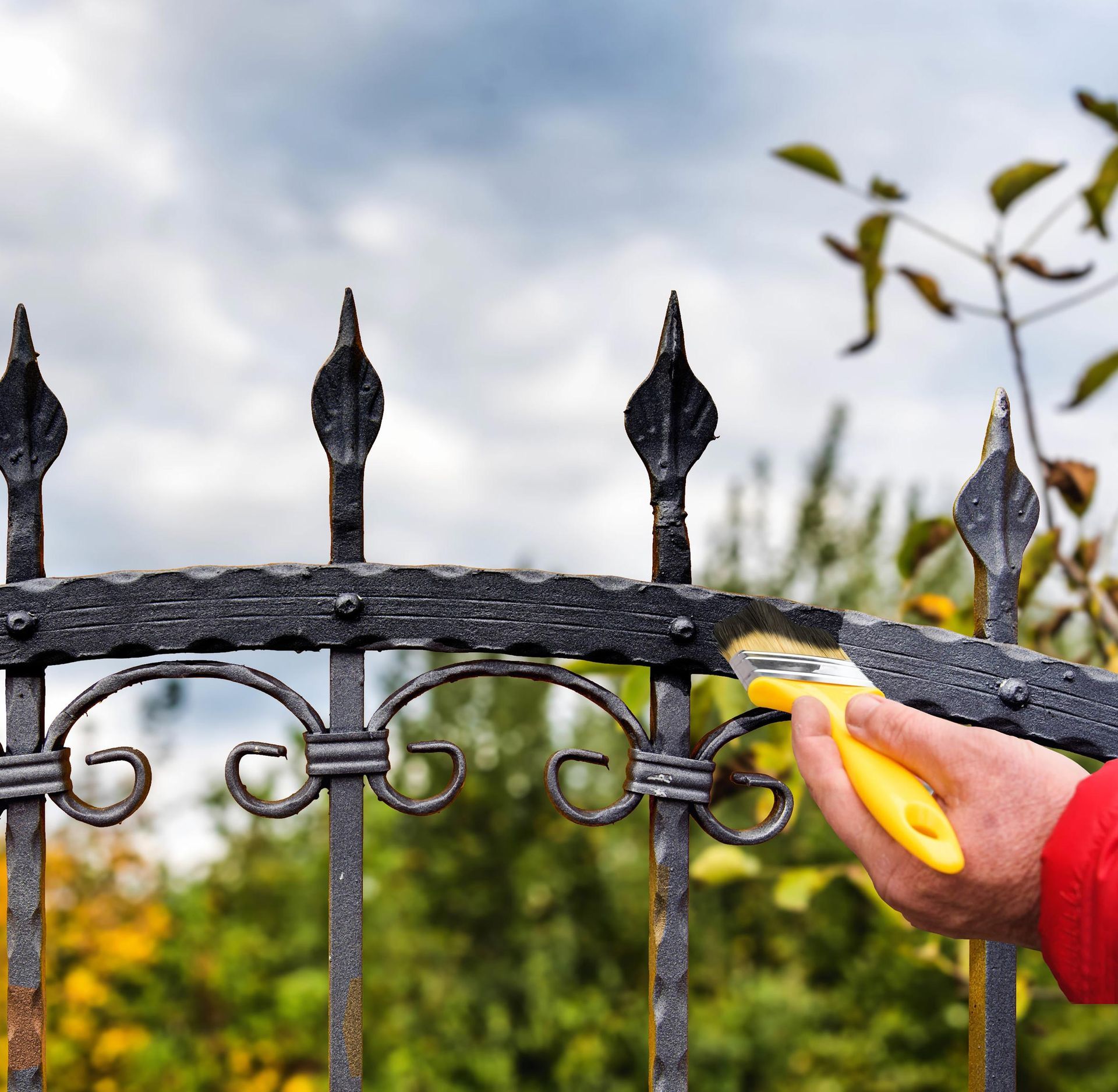 Person painting a black wrought iron fence with a yellow brush outdoors.