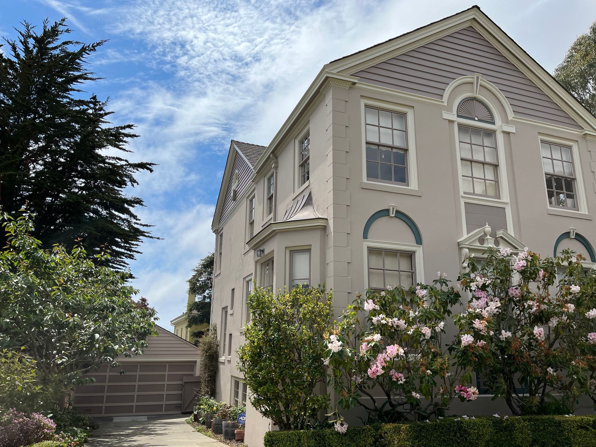 Person paints a stucco exterior wall with a roller, next to a white window.