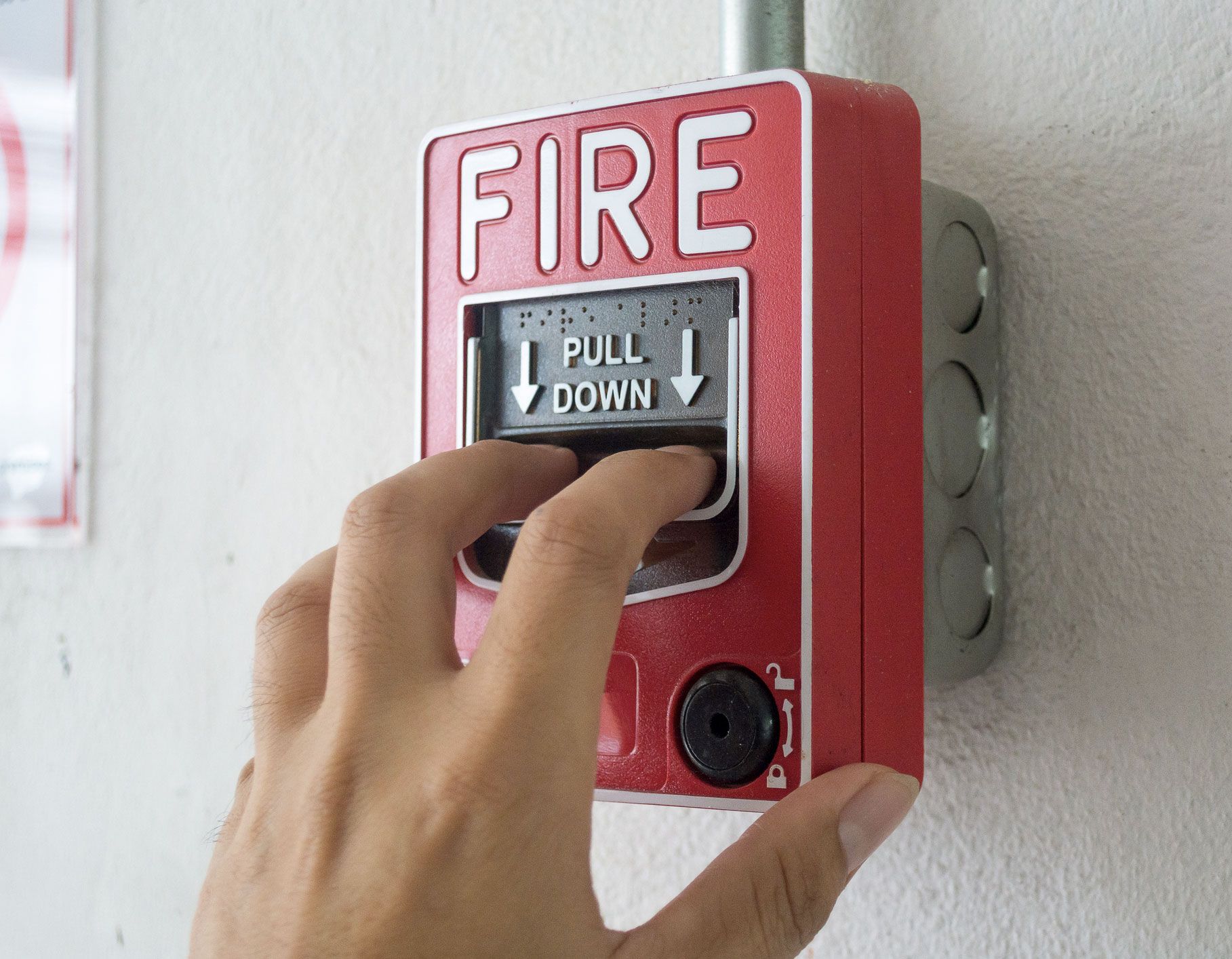 A hand is pressing a fire alarm on the wall. A hand is pressing a fire alarm on the wall.