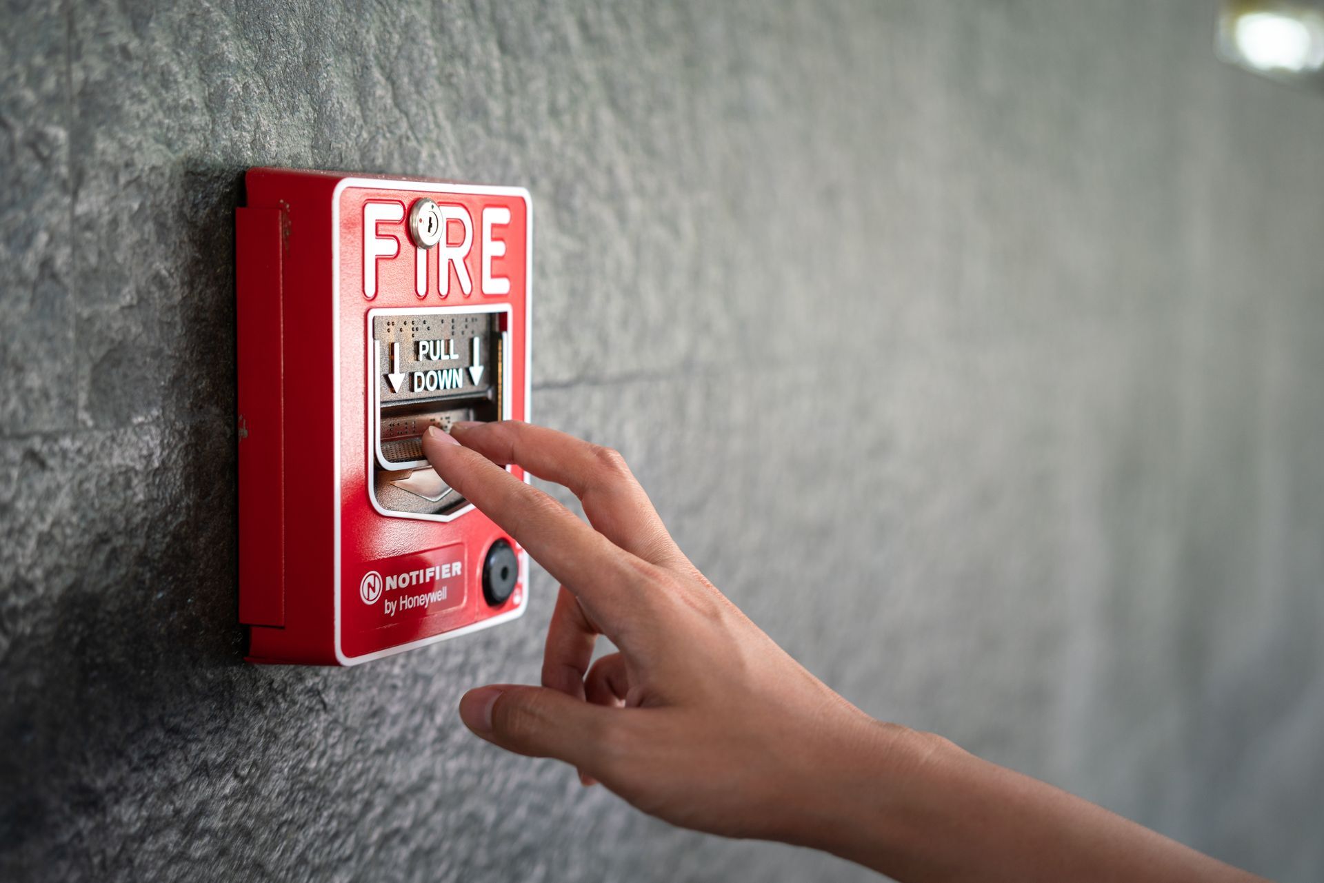 Person activating a manual pull station as part of building fire alarm systems for safety.