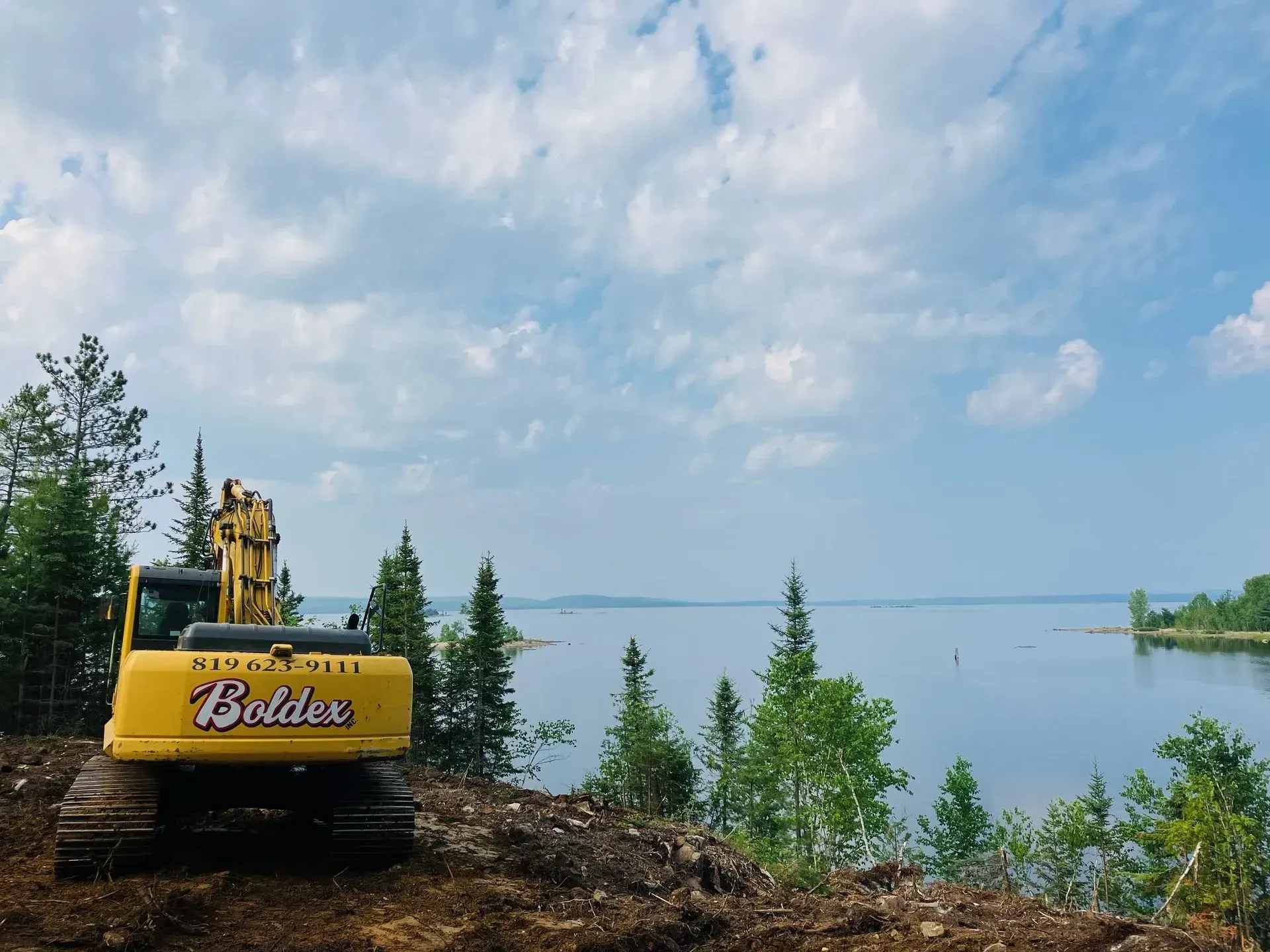 Une pelleteuse jaune surplombe un lac sous un ciel nuageux.