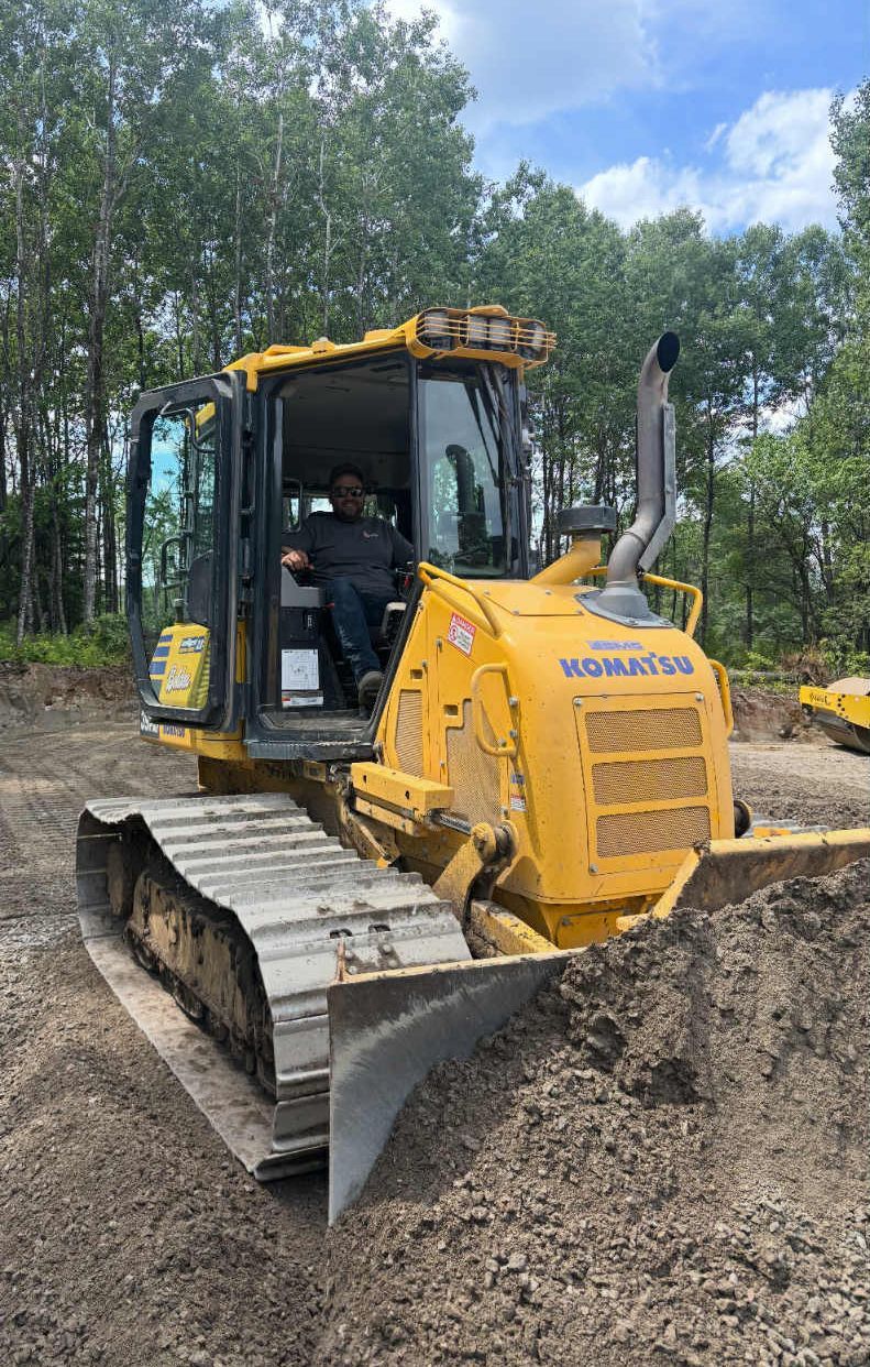Un bulldozer Komatsu jaune, avec une personne au volant, en action dans un champ de terre près d'arbres.