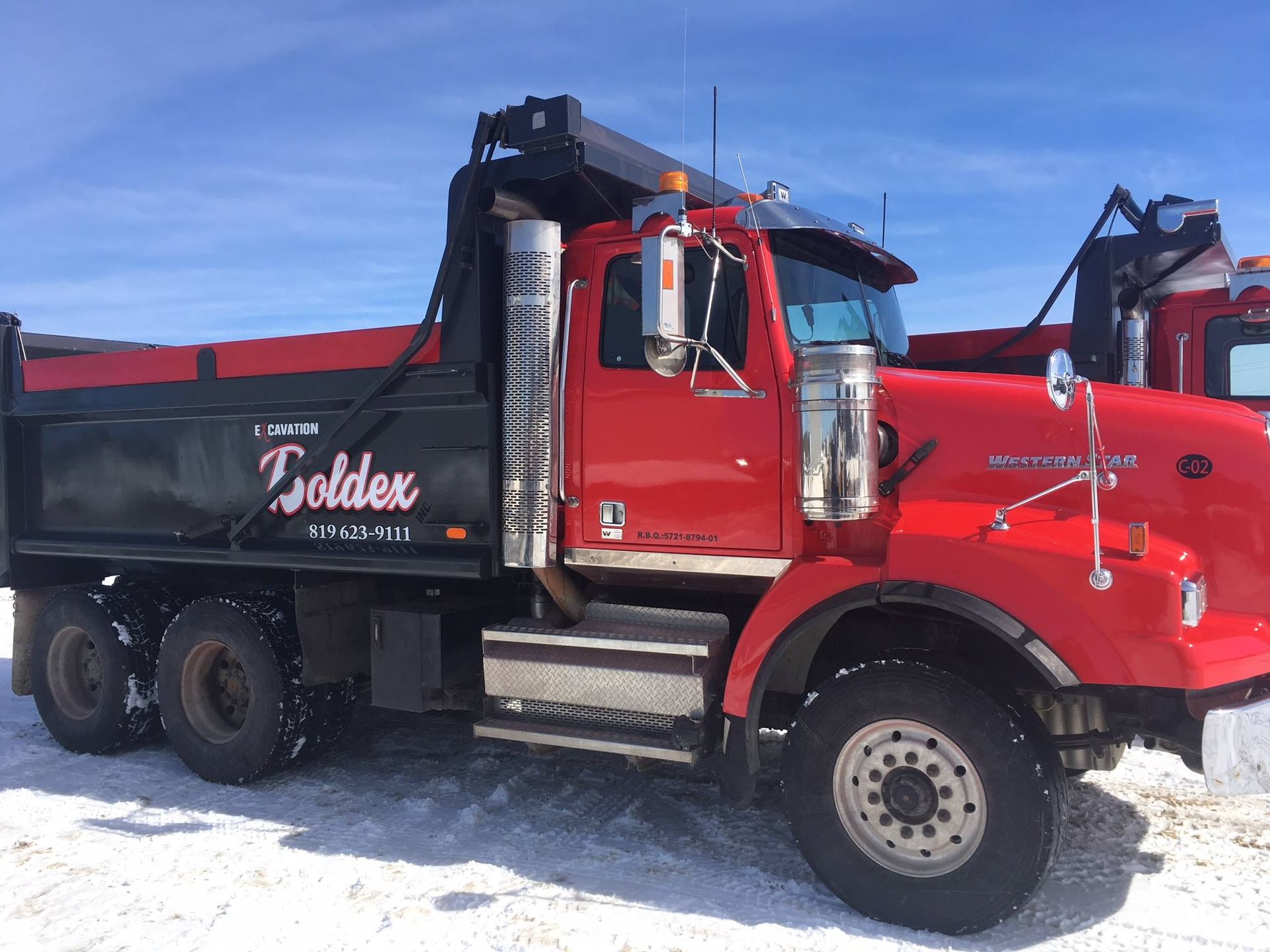 Camion-benne rouge dans la neige, arborant l'inscription « Goldenx » sur le côté, sur fond de ciel dégagé.