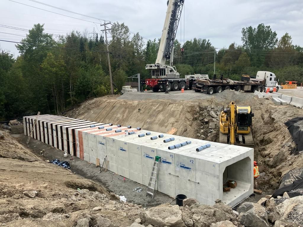 Un grand ponceau en béton est installé par une grue dans une excavation sur un chantier de construction.