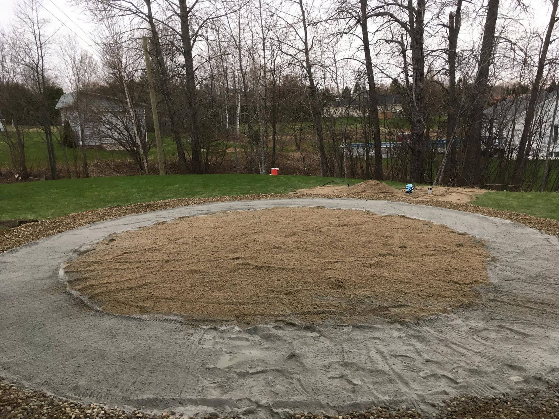 Allée circulaire en gravier et parcelle de terre nue avec fond d'herbe et d'arbres.