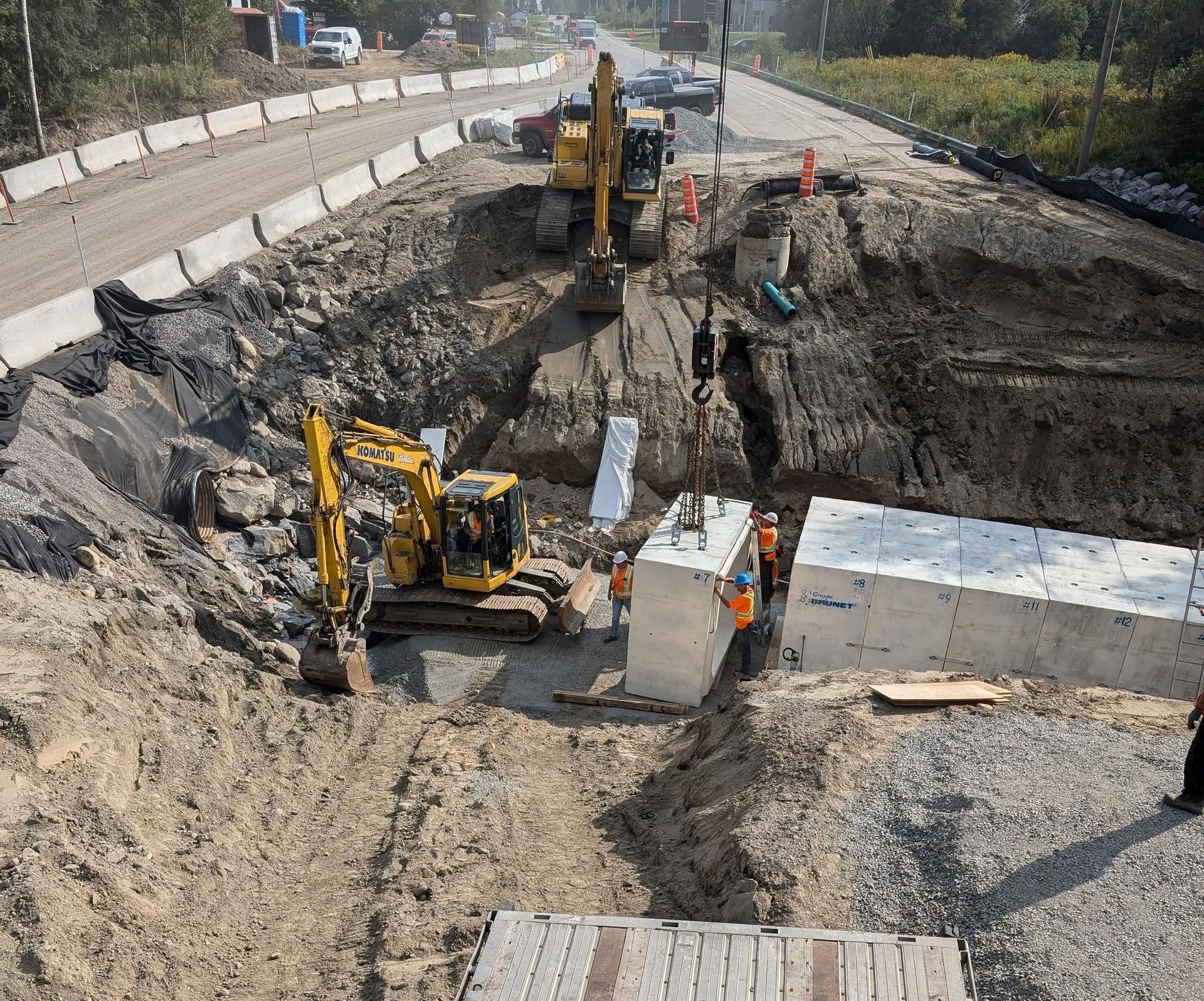 Chantier : des excavatrices travaillent dans une tranchée profonde, mettant en place des structures en béton pour des travaux routiers.