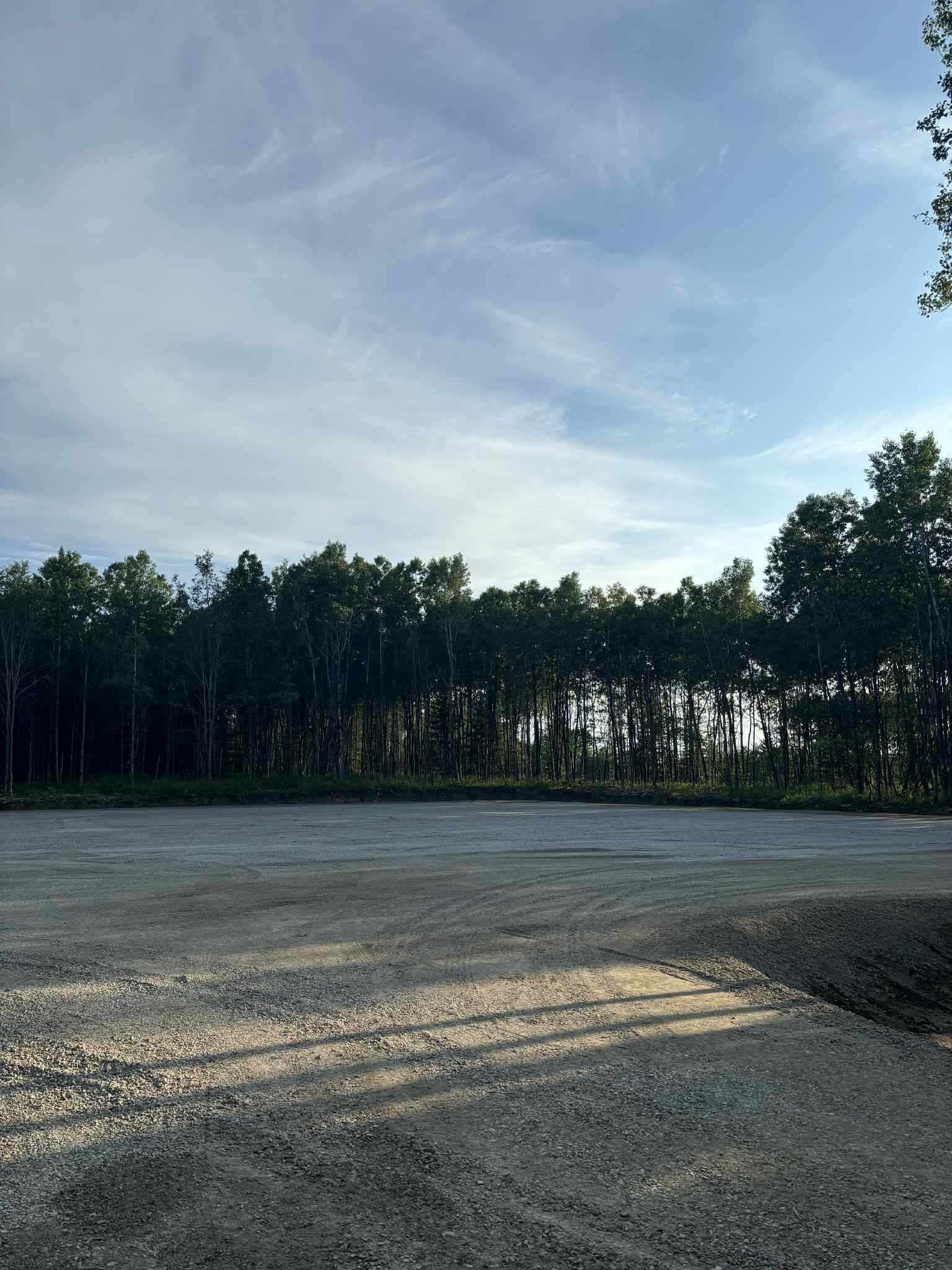 Au premier plan, une zone de gravier bordée d'arbres se détache sur un ciel bleu partiellement nuageux.