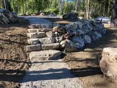 Marches en pierre et mur de soutènement menant à un chemin de gravier dans une zone boisée.