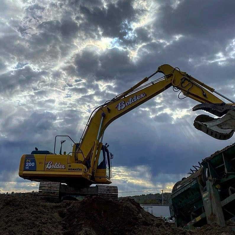 Une pelleteuse jaune travaille sur fond de ciel nuageux, à côté d'un conteneur vert.