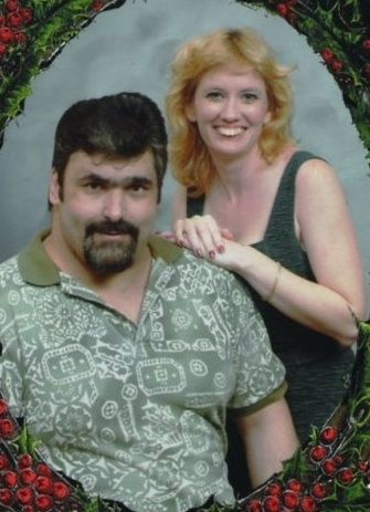 A man and woman posing for a picture with a wreath in the background