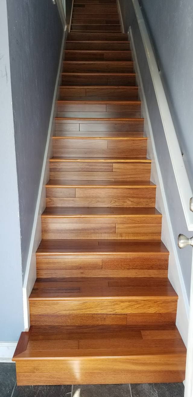 A steep, straight wooden staircase leads upward between two gray walls with white trim.