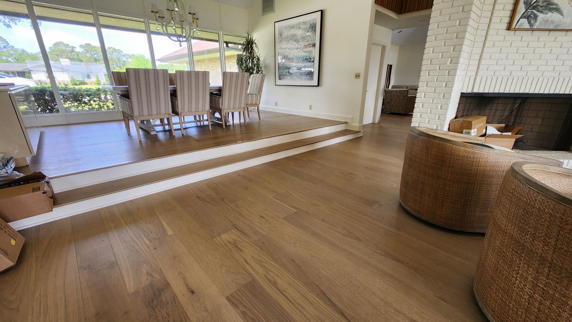 A modern living area with light wood flooring, a dining area on a raised platform, and textured round side tables.
