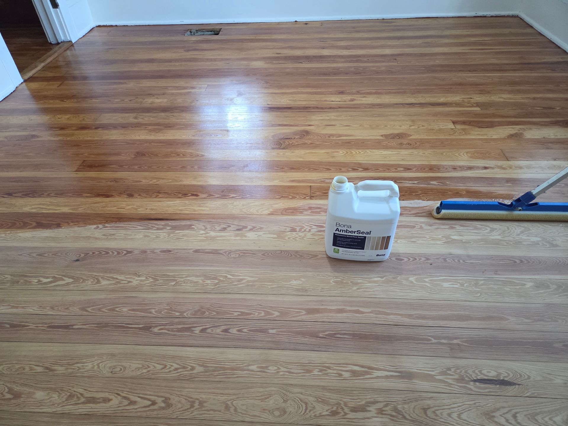 A wooden floor in the process of being stained, showing a clear divide between the raw wood and the dark finished area.