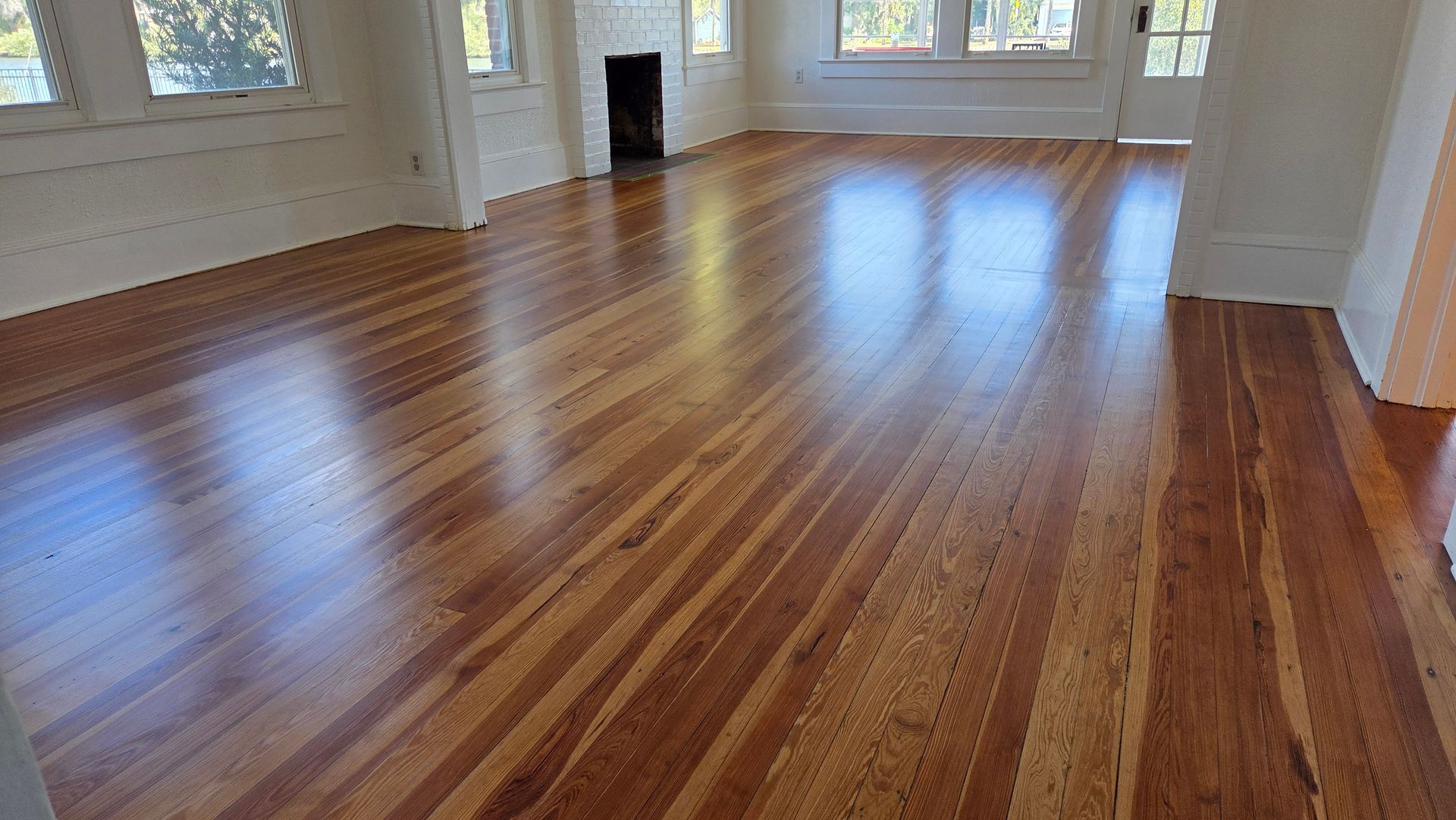 Polished, light-to-medium brown wooden floorboards stretch across a bright, empty room with white walls and trim.