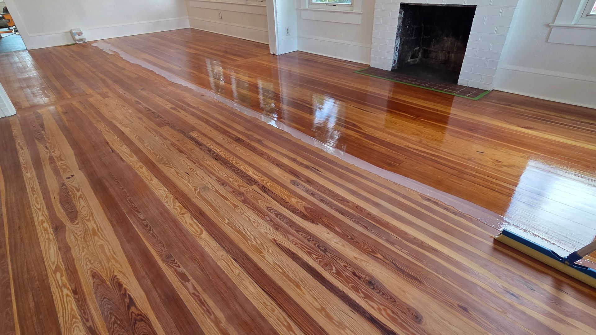 Polished, reddish-brown wood flooring in a room with a white fireplace and white walls.