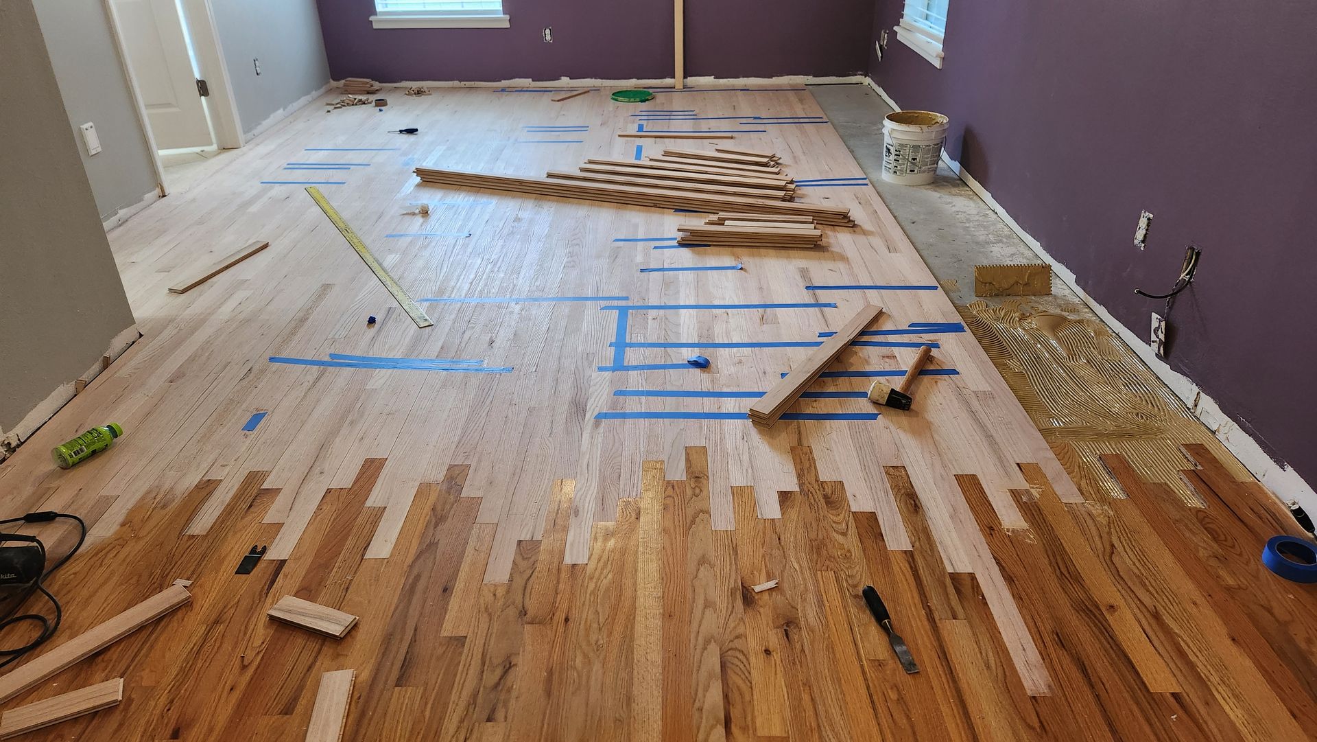 Hardwood floor in the process of being sanded, showing half-finished light wood and half-finished original brown wood.