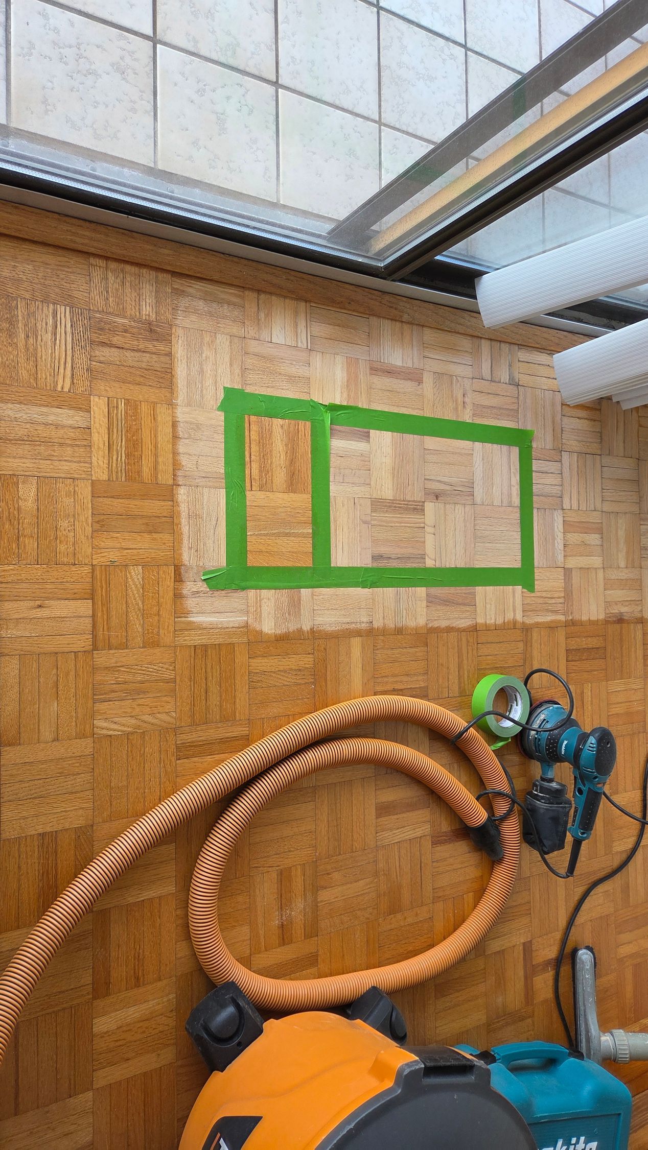 Green painter's tape forms two adjacent rectangular outlines on a light-colored, textured wood wall in a workshop.