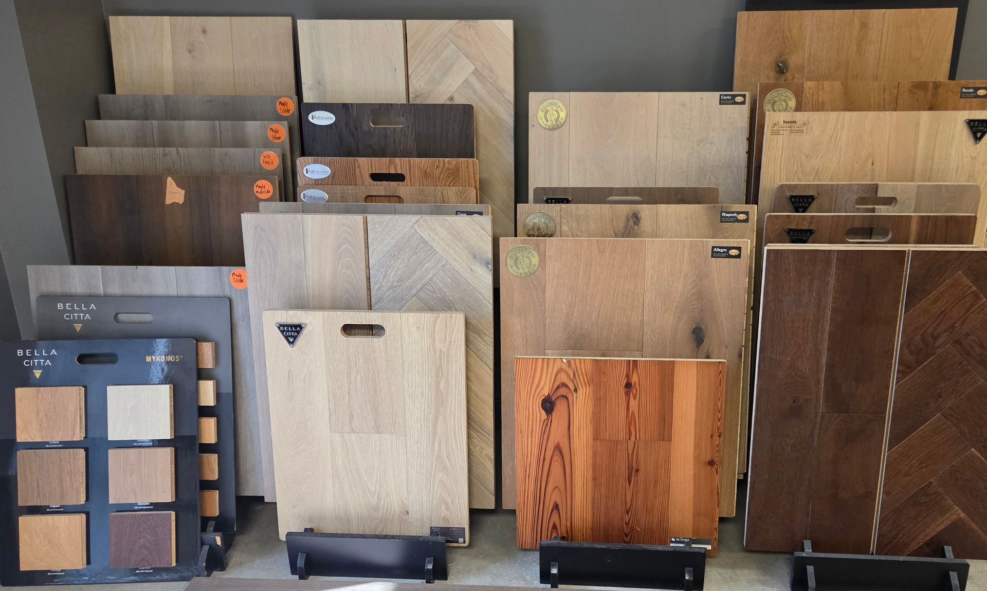 Display of various wood flooring samples in natural, brown, and gray tones arranged on store racks.